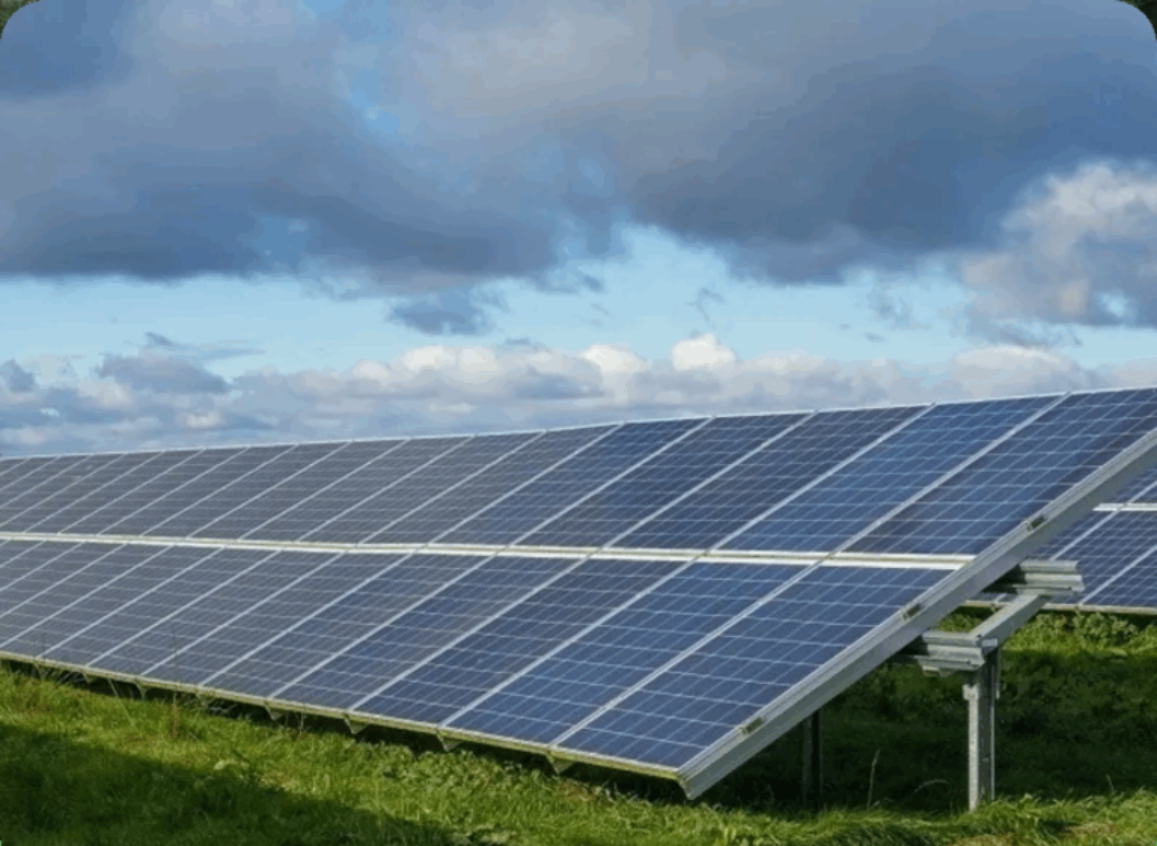 Solar panels under a cloudy sky on a green field.