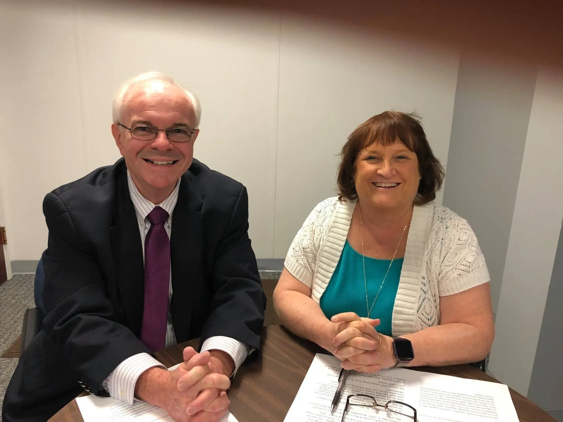 Two smiling professionals sitting at a table in a meeting room.