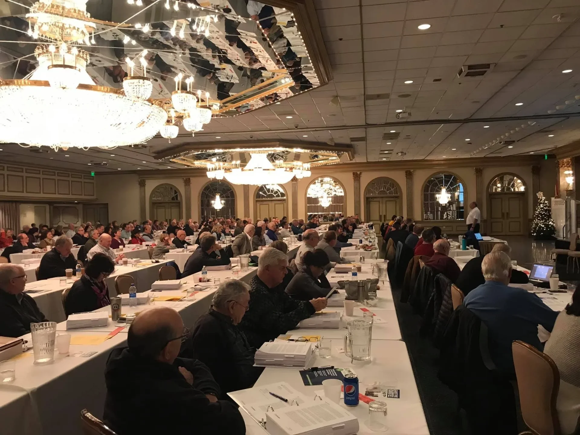 A large audience seated in a conference hall with chandeliers.