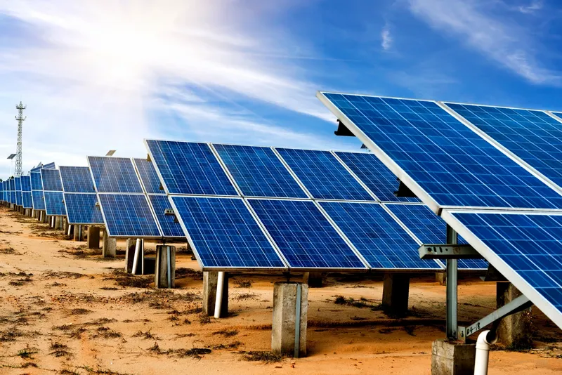 Solar panels arranged in a desert setting under a bright blue sky.