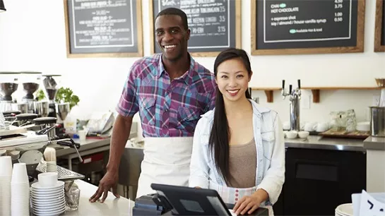 Two friendly cafe employees smiling behind the counter.